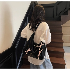 Dettaglio borsa hobo nera lucida con fiocchi in seta rosa e cuori di perle indossata a spalla