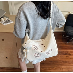 Detail of white canvas crossbody bag featuring cartoon cat embroidery and plush cloud charm