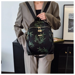Détail du sac à dos en nylon noir avec motif de feuilles vertes et fermetures éclair dorées