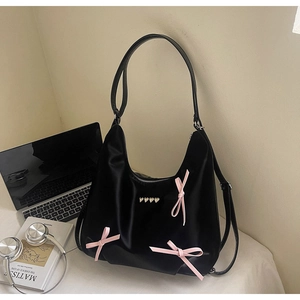Dettaglio della borsa hobo nera con fiocchi di nastro rosa e borchie a cuore dorate su raso