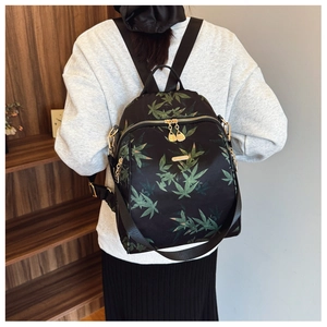 Détail d'un sac à dos noir avec imprimés feuilles vertes et fermetures éclair dorées