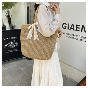 Detail view of woven straw tote bag featuring white lace bow and leather shoulder straps