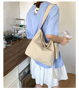 Beige canvas tote bag with wide strap detail shown in a casual lifestyle setting