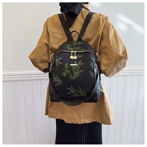 Détail d'un sac à dos imprimé avec motifs de feuilles vertes et fermeture éclair dorée