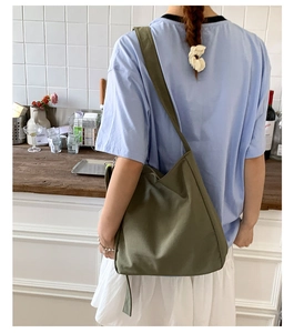 Back view of a large olive green canvas tote bag worn by a woman in a kitchen setting