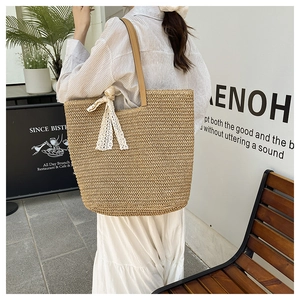 Outdoor shot of a woven straw tote bag with leather handles and white lace bow detail