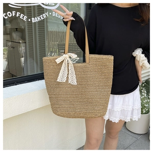 Detail of hand-woven straw tote bag with brown leather handles and white lace bow