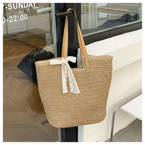 Close-up of handmade straw tote bag featuring white lace bow and brown leather handles