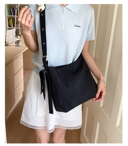 Detail of black canvas shoulder bag showing the wide strap with silver metal eyelets