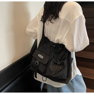 Rear view of model wearing black nylon crossbody bag with multi-pocket and drawstring detail