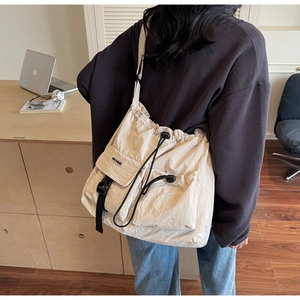 Detail of beige nylon crossbody bag featuring drawstring closure and multi-pocket design