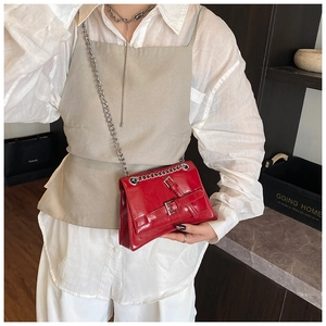 Gros plan d'un sac carré rouge brillant avec chaîne et boucles porté par un mannequin