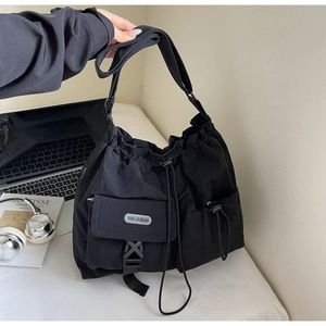 Detail of a black nylon crossbody bag with drawstring closure and functional front pockets