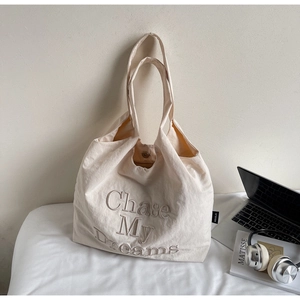 Détail du lettrage brodé 'Chase My Dreams' sur un sac fourre-tout en toile beige de qualité