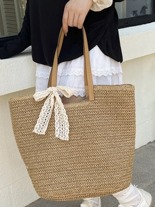 Handwoven straw tote bag with brown leather handles and delicate white lace bow detail