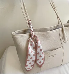 Detail of beige lychee leather tote bag featuring a pink polka dot silk scarf on handle