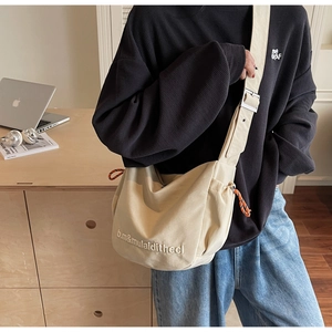 Detail of off-white canvas crossbody bag with adjustable wide strap and side drawstrings
