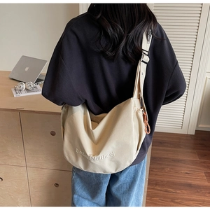 Detail of beige canvas crossbody bag with letter embroidery and orange zipper pull