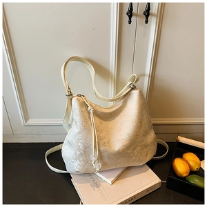 Detail of cream jacquard tote bag with floral embossing and drawstring bead on a book