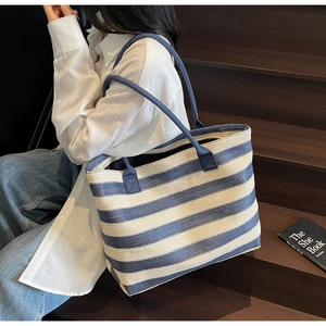 Blue and white striped woven straw tote bag held by a model on wooden stairs