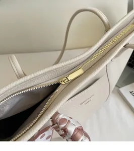 Close-up of beige lychee grain leather tote bag with gold zipper and polka dot silk scarf