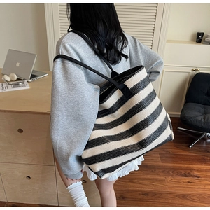 Detail of a large woven tote bag with black and beige stripes on a female model