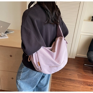 Close-up of light purple nylon messenger bag with letter embroidery and side label
