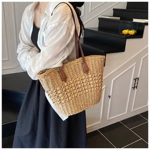 Detail view of woven straw tote bag with brown leather straps held by a model on shoulder