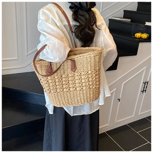 Detail of hand-woven straw tote with premium brown leather straps on a shoulder