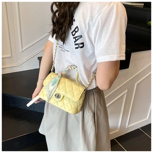 Detail of yellow quilted crossbody bag with silk scarf handle and metal twist lock