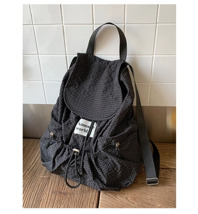Details des schwarzen Rucksacks mit Gittermuster, Kordelzug und Klappe auf Holzoberfläche