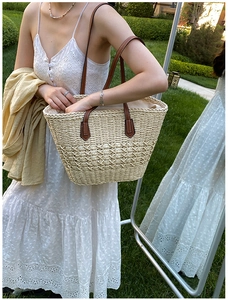 Detailed view of woven paper straw tote with brown leather handles on a summer lawn
