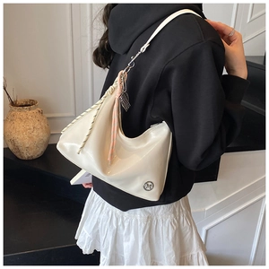 Detail of white glossy tote bag with braided cord trim and metal logo worn by a model