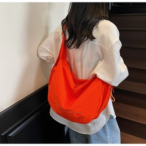 Detail of orange canvas crossbody bag featuring letter embroidery and drawstring design