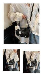 Détail du sac croissant en cuir verni noir avec charme de perles blanches et ruban