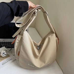 Detail view of large beige canvas hobo bag with wide strap and side orange rope detail