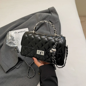 Detail view of black quilted leather bag with silver chain and skull charm