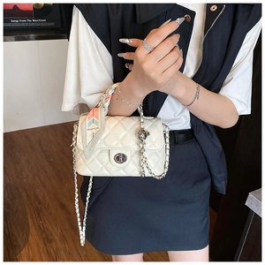 Detail of white quilted handbag featuring a metal lock and silk scarf wrapped handle