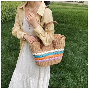 Detailed close-up of handmade straw tote bag with multi-colored woven stripes on green grass