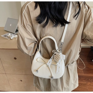 Détails du nœud et breloque cœur perle sur sac demi-lune en cuir crème élégant