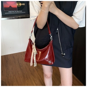 Detail of red glossy patent leather tote bag with silver hardware and woven tassel charms