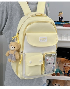 Detail of a cream yellow school backpack featuring a plush bear charm and clear display pocket