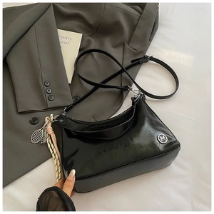 Detail of glossy black tote bag featuring a silver M logo and tennis racket charm