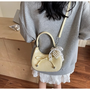 Détail d'un sac demi-lune jaune crème avec nœud décoratif et pendentif cœur perlé
