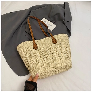 Close-up of beige straw tote bag with intricate hollow weave and brown leather handles