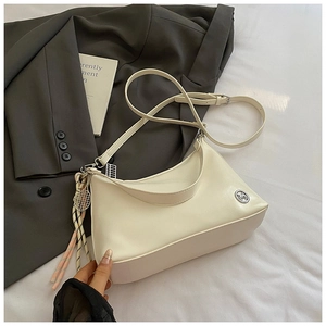 Detail of a creamy white hobo bag with striped scarf decor and circular metal logo plaque