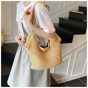 Detail of hand-woven straw shoulder bag with contrast yellow leather trim on a model