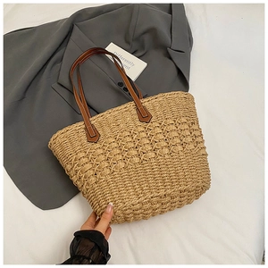 Detail of the woven straw tote bag featuring a leather handle and hollow pattern design