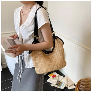 Detail of woven straw tote bag featuring black leather shoulder straps and refined trim