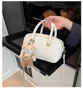 Detail of white leather handbag with plush bear charm and embossed logo on front